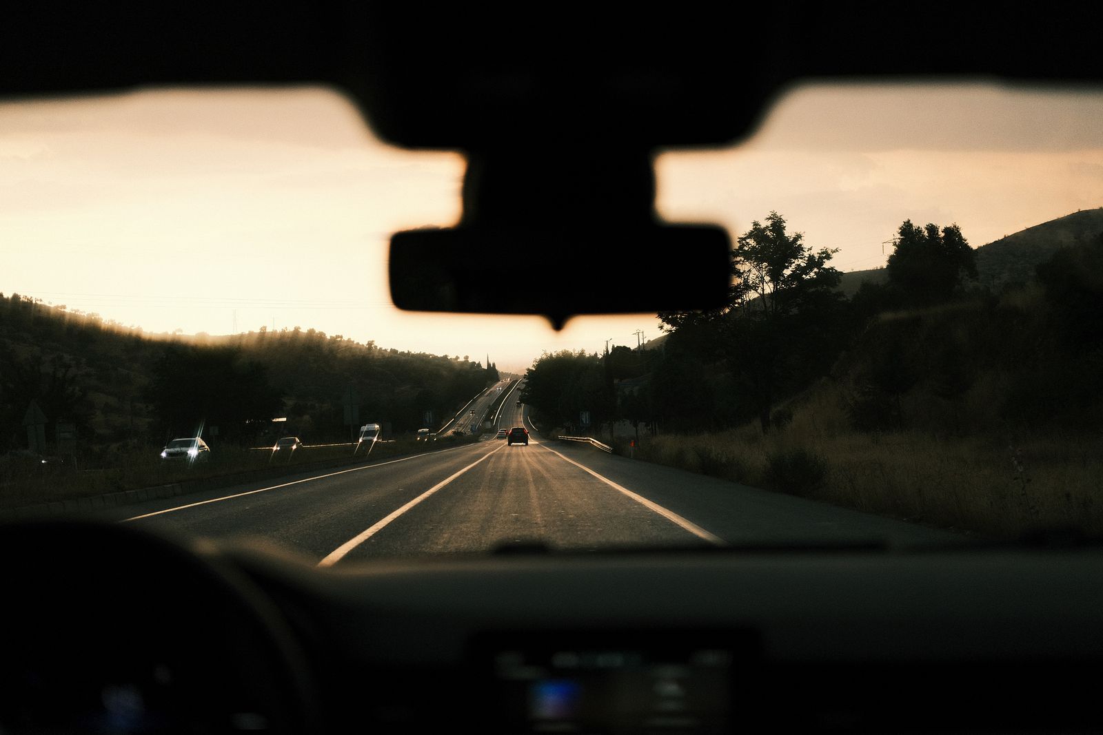 A highway seen through a car's windshield near the rearview mirror at dusk, the kind of view a dash cam records