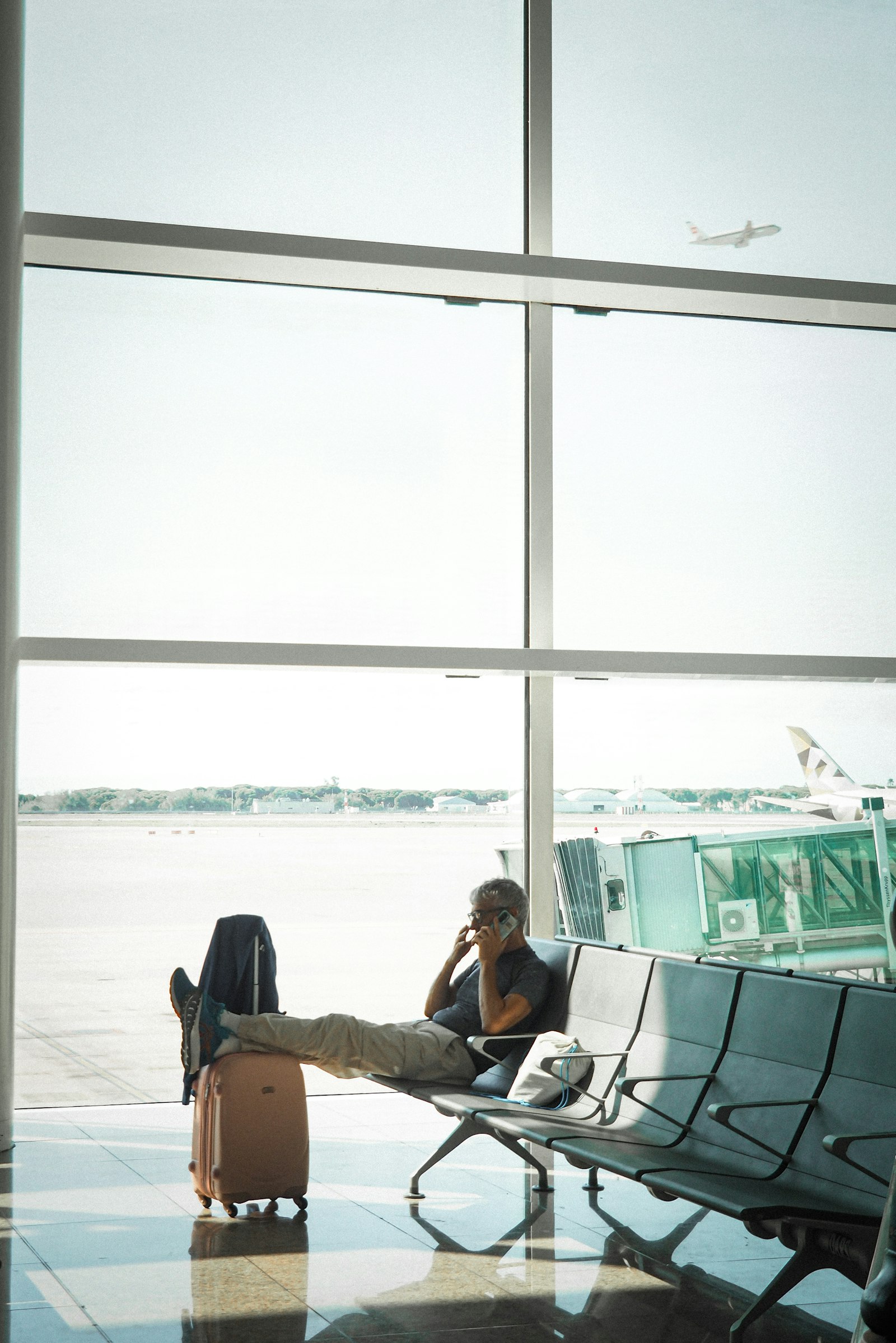 Traveler on a smartphone in an airport departure lounge, suitcase beside the seat