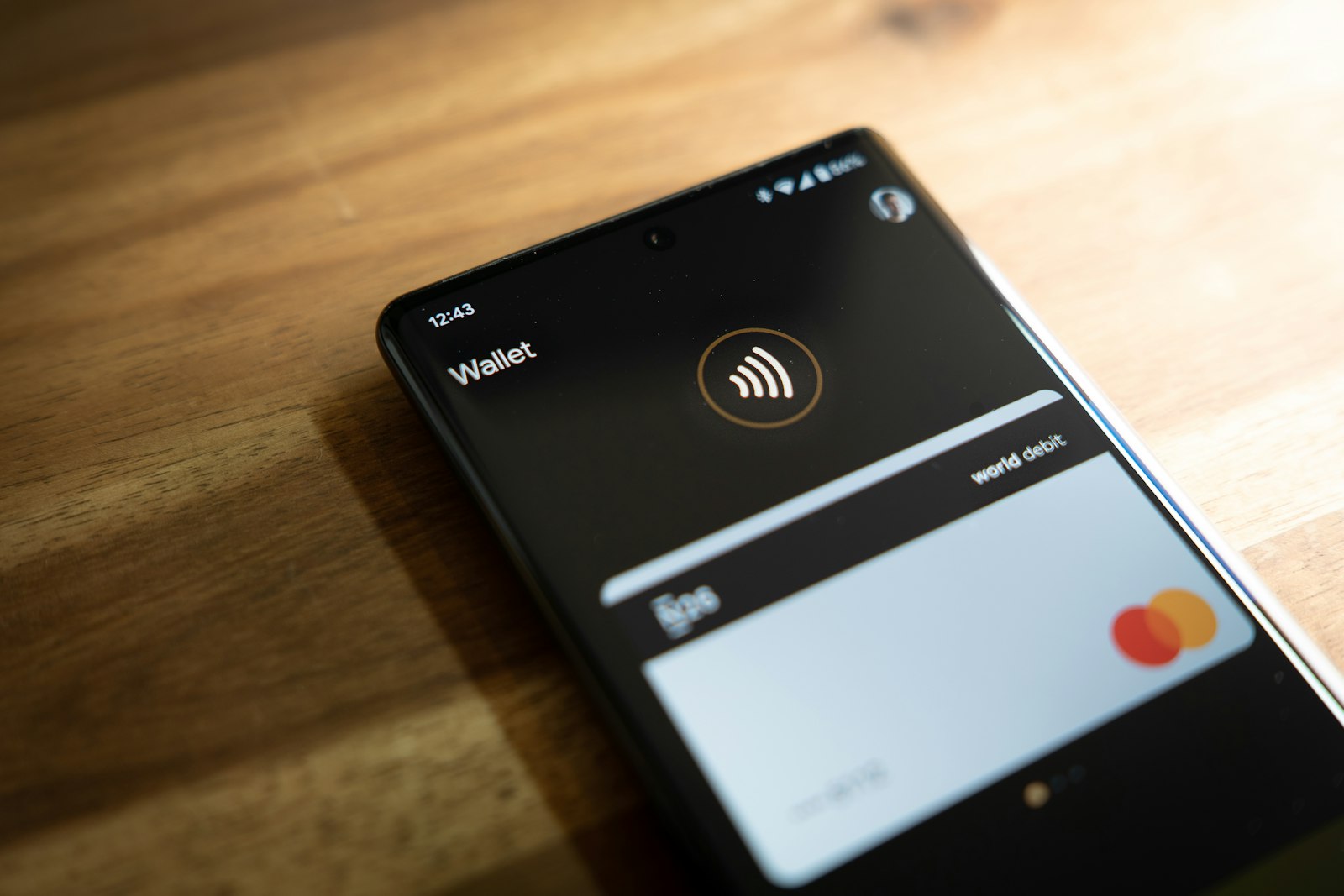 Смартфон на деревянном столе с открытым приложением Wallet и банковской картой на экране