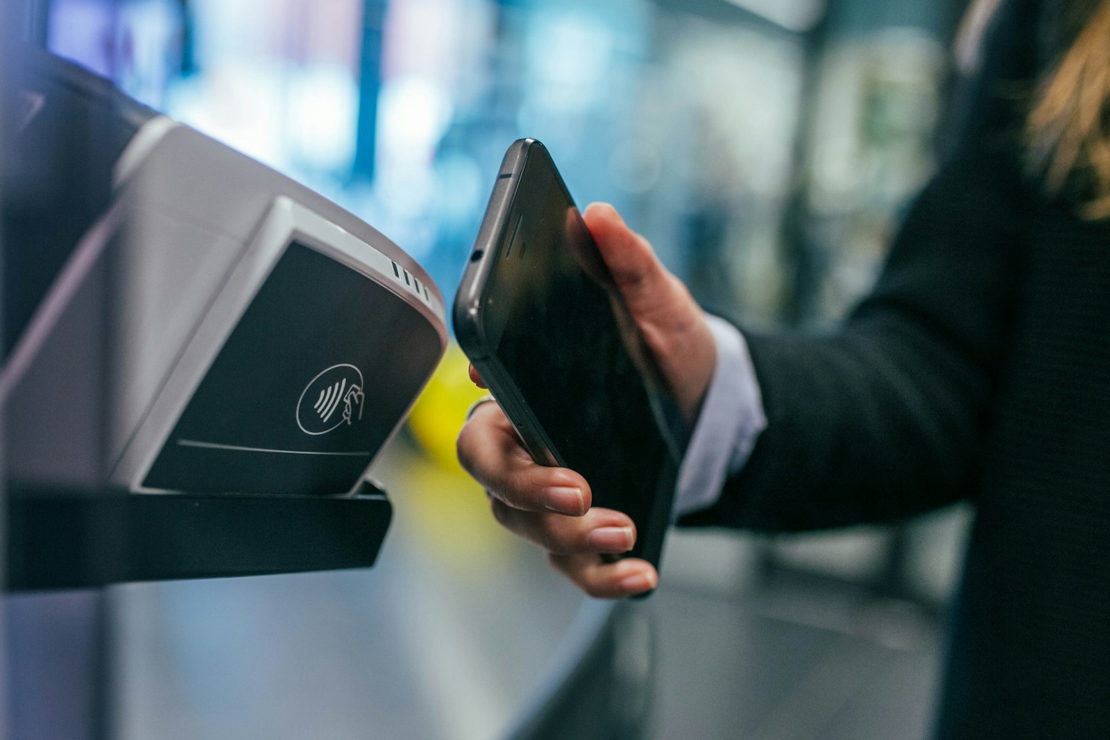 A smartphone held near a contactless payment terminal with the NFC symbol visible on the reader