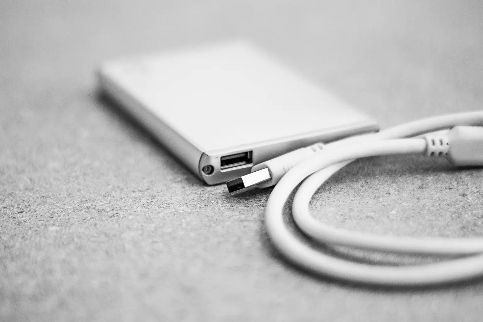 A portable external SSD drive with a USB-C cable coiled beside it on a desk