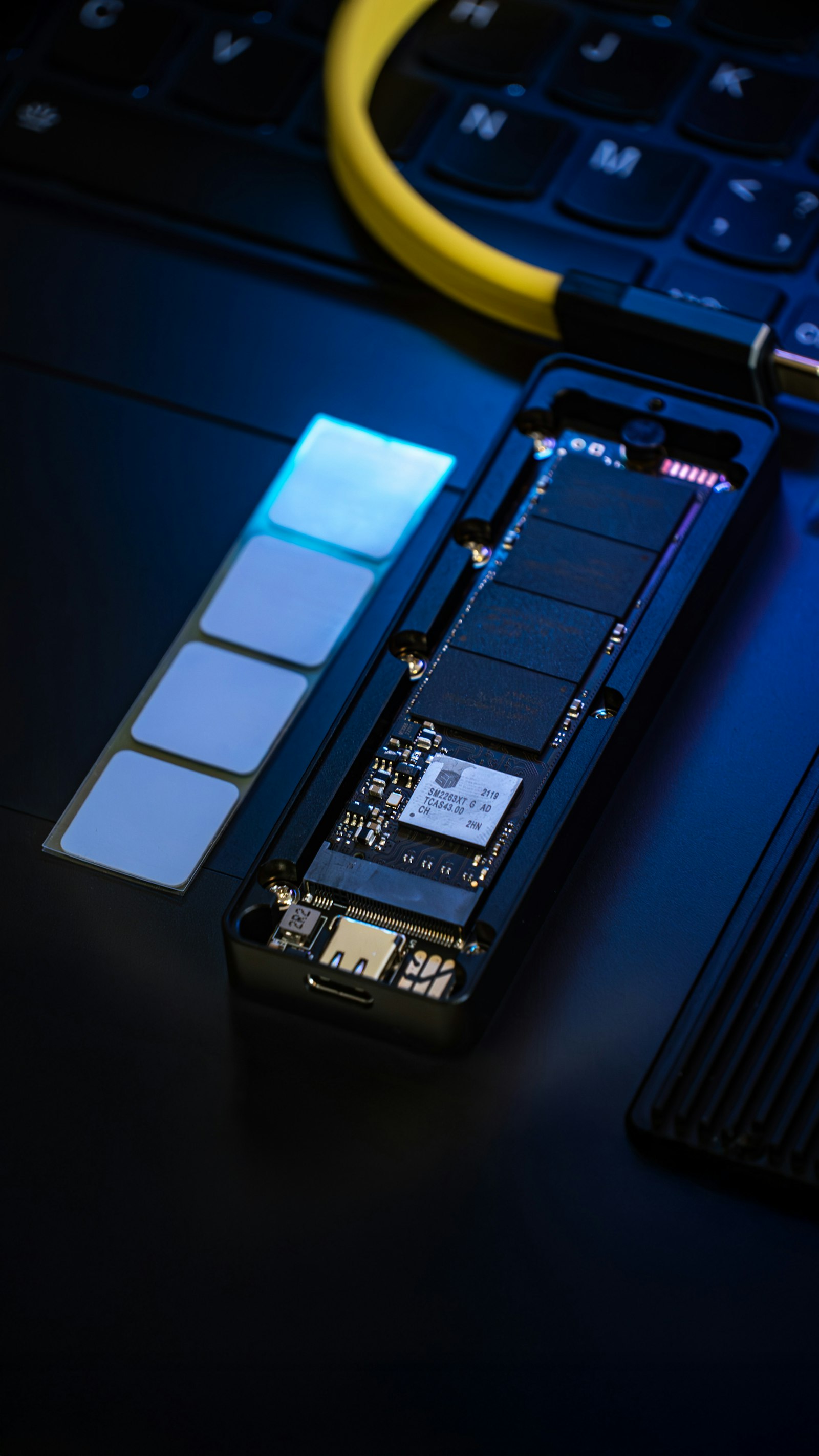 Жёлтый кабель USB-C подключён к разобранному корпусу портативного SSD на фоне клавиатуры ноутбука